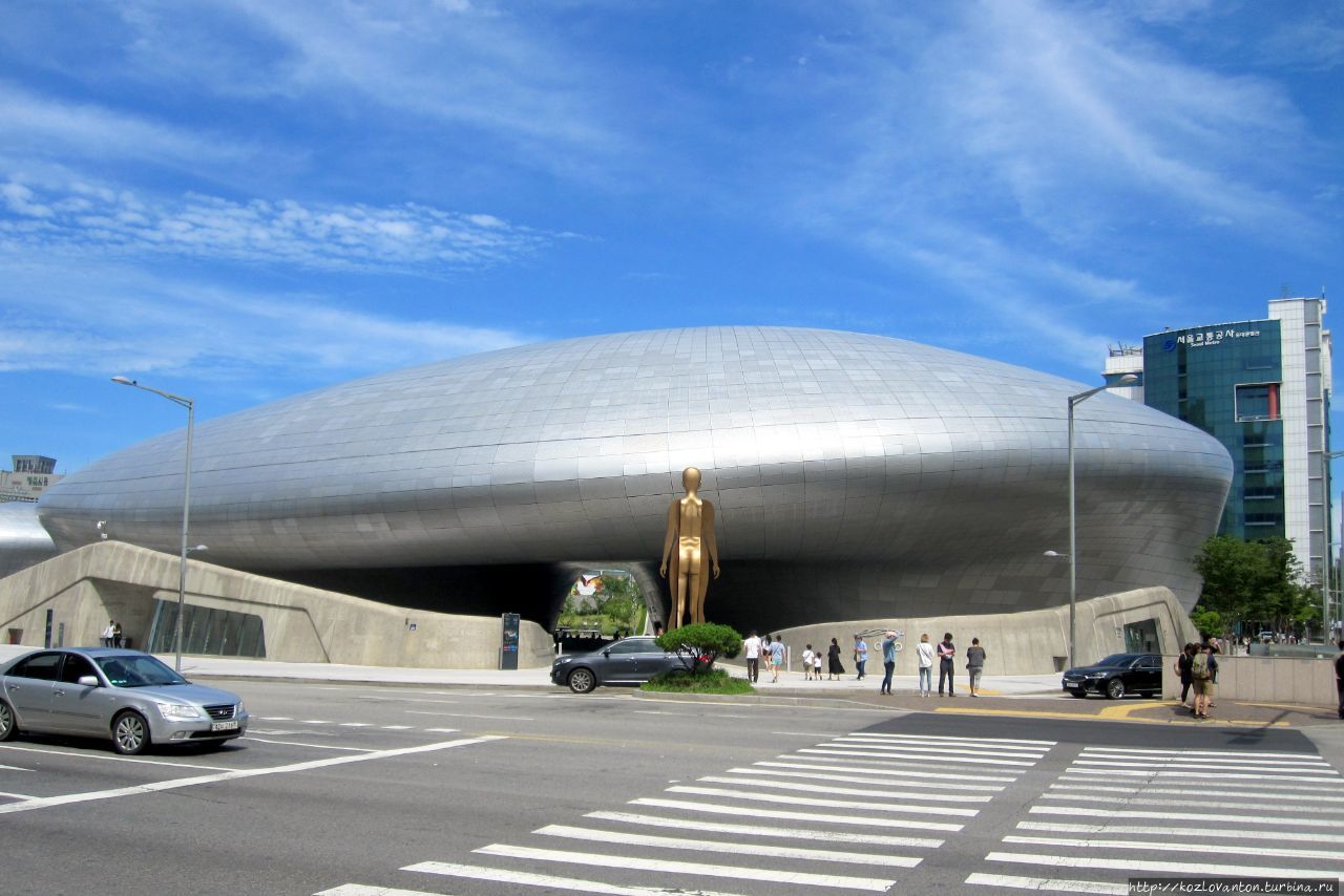 По диагонали через дорогу от него недавно открылось подлинное архитектурное украшение Сеула — торгово-выставочный комплекс Тондемун дизайн плаза. А всего лишь 10 лет назад здесь были неприглядные бейсбольный и футбольный стадионы, под трибунами которых раскинулась большая барахолка. Сеул, Республика Корея По диагонали через дорогу от него недавно открылось подлинное архитектурное украшение Сеула — торгово-выставочный комплекс Тондемун дизайн плаза. А всего лишь 10 лет назад здесь были неприглядные бейсбольный и футбольный стадионы, под трибунами которых раскинулась большая барахолка. Сеул, Республика Корея