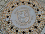 Герб города на канализационном люке, на гербе — синичка  и дата получения городского статуса