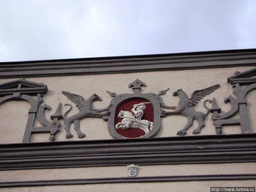 Наверху Погоня — герб Литвы, поддерживаемый двумя крылатыми львами — грифонами, ниже рельефная голова Гермеса в крылатом шлеме Вильнюс, Литва