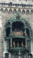 На центральной башне ратуши установлены часы-куранты, разыгрывающие 15-минутное представление. Ежедневно в 11 часов начинают бить 43 ратушных колокола, открываются окна, и 32 фигуры, высотой в человеческий рост, начинают разыгрывать сценки из городской жизни, которые происходили на Мариенплац. Герцог Вильгельм V и его жена Рената Лотарингская открывают рыцарский турнир, проходивший на площади в 1568 году в честь их свадьбы. Перед ними проходят герольды с трубами, знаменосцы и оруженосцы, закованные в доспехи конные рыцари. По сигналу герцога они мчатся друг на друга и рыцарь с баварским щитом выбивает из седла лотарингского рыцаря. Вслед за турниром дирижёр взмахом палочки открывает на нижней части часов танец бондарей в ярко-красных куртках, которые празднуют отступление чумы в 1517 году. Представление проходит зимой в 11 часов, а летом также в 12 и в 17 часов. (википедия)