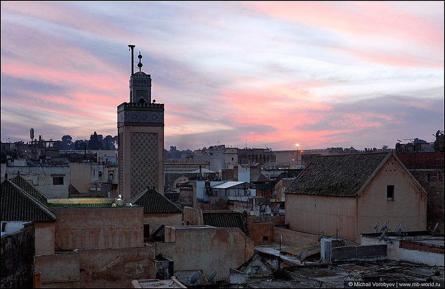 Возвышающийся минарет мечети над крышами жилых домов Фес, Марокко