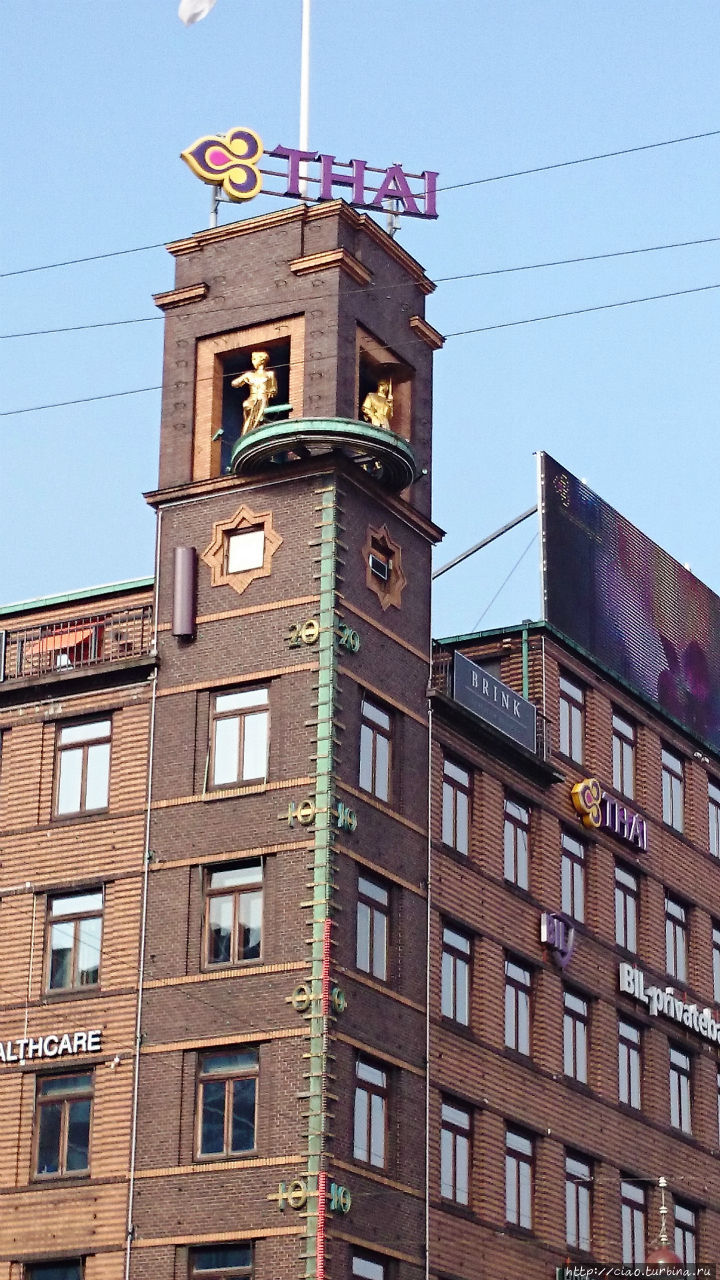 Необычно: на углу здания находится огромный термометр, а наверху две фигуры – девушка на велосипеде и девушка с зонтиком. В зависимости от погоды видна одна из них. Копенгаген, Дания