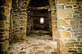 Вход в храм закрыт железной решеткой, но через нее просматривается каменный зал храма, у противоположной стены виднеется каменная купель и лежащий за ней крест.