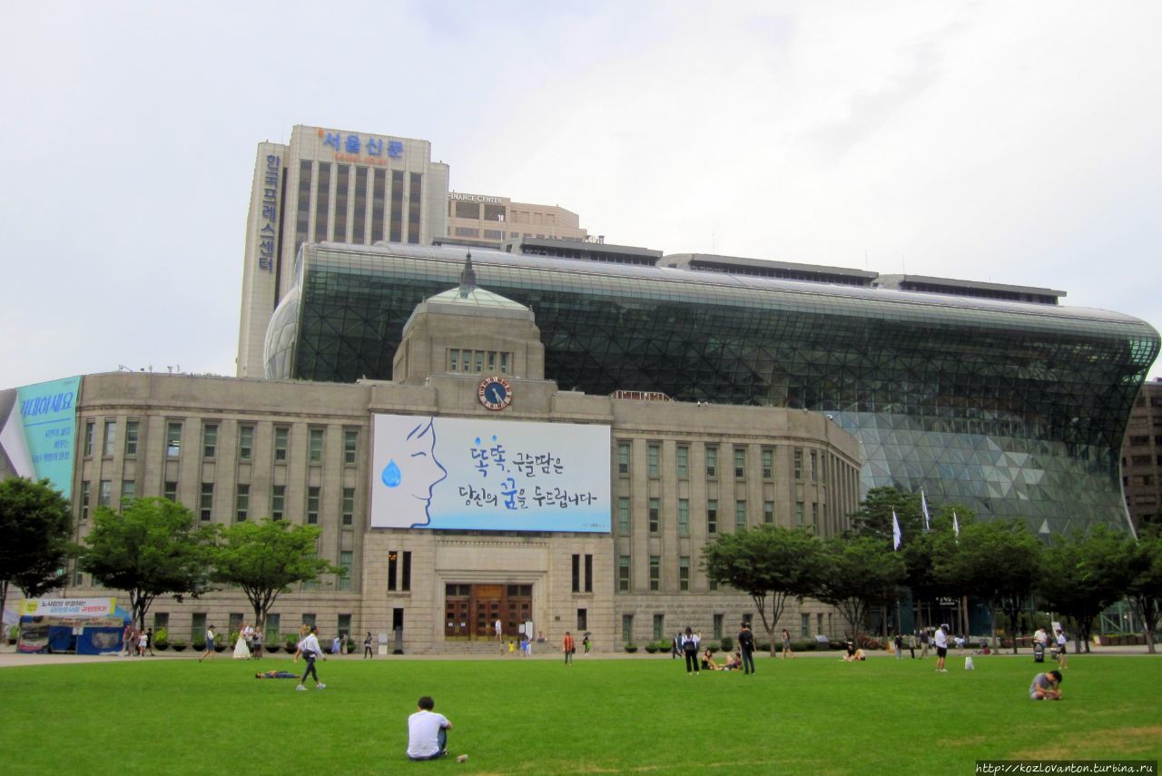 Площадь у Сити-холла — самый центр города. Впереди — старое здание мэрии, построенное при японской оккупации в 1926 году (ныне здесь — библиотека) и за ним 
новое 13-этажное строение для мэрии, построенное уже после 2008 года. Сеул, Республика Корея