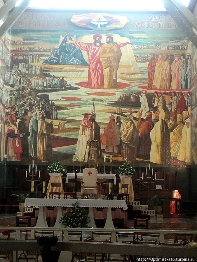 Грандиозное мозаичное панно, расположенное на задней стороне пресвитерии. Главная его идея — объединение человечества в любви и равенстве под покровительством Вселенской Церкви. Над всем и вся — Бог Отец, присутствие которого символизируется Всевидящим оком. Святой Дух в виде парящего голубя и Сам Бог Сын, Иисус, стоящий на Сионе с распростёртыми руками и призывающий всех под Свои длани.

  «Придите ко Мне, все нуждающиеся и обременённые, и Я успокою вас; возьмите иго Моё на себя и научитесь от Меня, ибо Я кроток и смирен сердцем, и найдёте покой душам вашим; ибо иго Моё благо, и бремя Моё легко». («От Матфея» 11:28/30).

    Рядом с Иисусом сидит Богородица, а по другую сторону стоит Пётр. Тот, которому было сказано:

     «И Я говорю тебе: ты — Пётр, и на сем камне Я создам Церковь Мою, и врата ада не одолеют её. И дам тебе ключи Царства Небесного; и что свяжешь на земле, то будет связано на небесах; и что разрешишь на земле, то будет разрешено на небесах». («От Матфея» 16:18/19).

   За Петром — остальные апостолы, Папы — миротворцы ХХ века, духовенство и нескончаемый поток мирян со всех стран всех континентов, объединённые лозунгом Никео — Цареградского символа веры: «Верую в единую, святую, соборную и апостольскую Церковь».