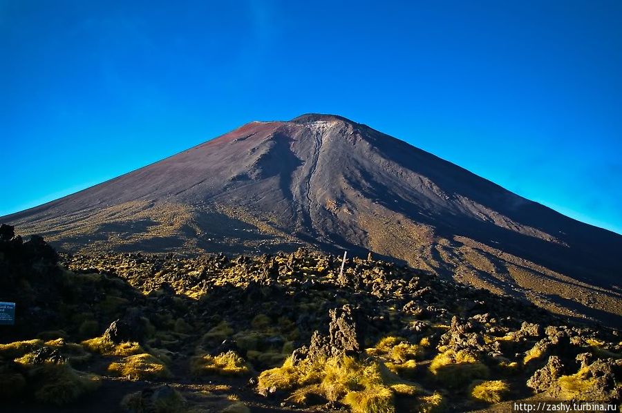 20-и километровый участок, которые известен под названием Tongariro alpine crossing (альпийский перевал Тонгариро). Трек этот очень популярен как среди местных, так и среди туристов, поэтому я стартовал еще до рассвета, чтобы избежать толп.
После первого резкого подъема я на рассвете оказался у подножья вулкана Нгаурухое. Национальный парк Тонгариро, Новая Зеландия