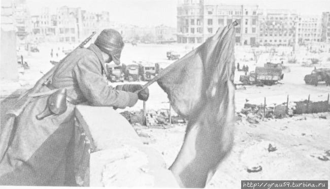 Красный флаг над площадью Павших борцов освобожденного Сталинграда. На заднем плане: здание универмага. На площади: захваченные советскими войсками немецкие грузовики.