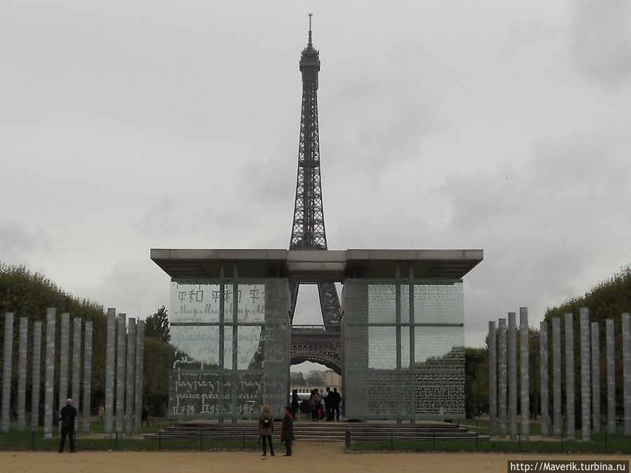 Перед Эйфелевой башней расположена стеклянная стена. На ней написано одно лишь слово МИР на многих языках. Париж, Франция