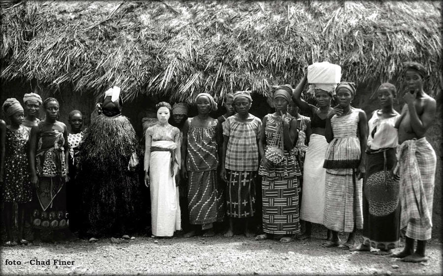 Bondo Initiate in White Kaolin at Bitema in Nongowa Chiefdom — 1969.
In the center is a young Bondo initiate covered in a white clay during one of the stages of her initiation. To her right is the Bondo Masquerade which was known locally as the Bondo Devil.
Location : Bitema Nongowa — Kenema District — Eastern Province Северная провинция, Сьерра-Леоне