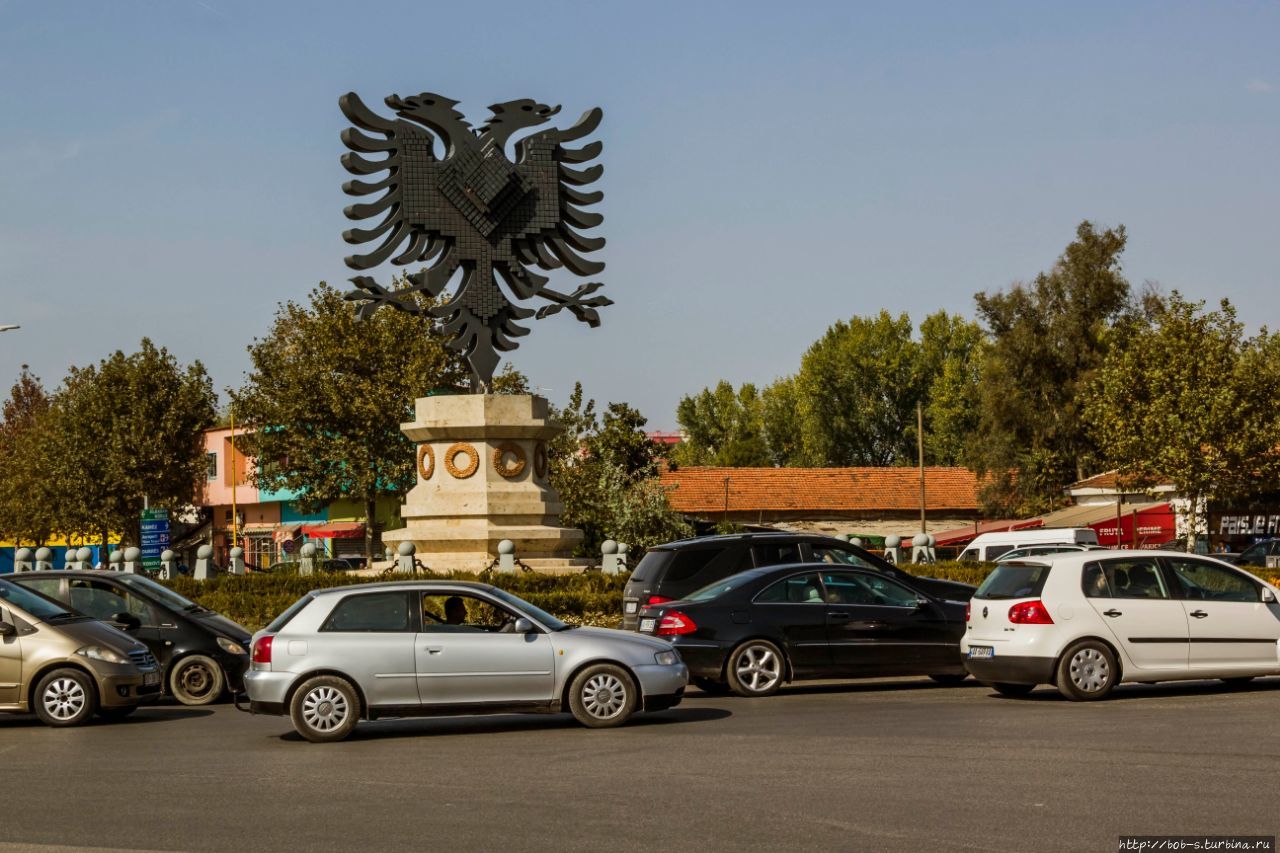 Перекрёсток который в народе называют просто — Площадь с Орлом. Рядом с ним как раз и находится так называемая Южная автостанция от которой можно укатить по Албании, кроме северной её части. В Шкодер отправляются от другой автостанции, она недалеко от этой, ближе к центру по той же улице. Тирана, Албания