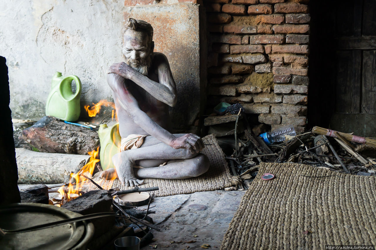 Садху наносит на тело пепел священного костра, смешанный с водой. После чего высыхает у костра Катманду, Непал