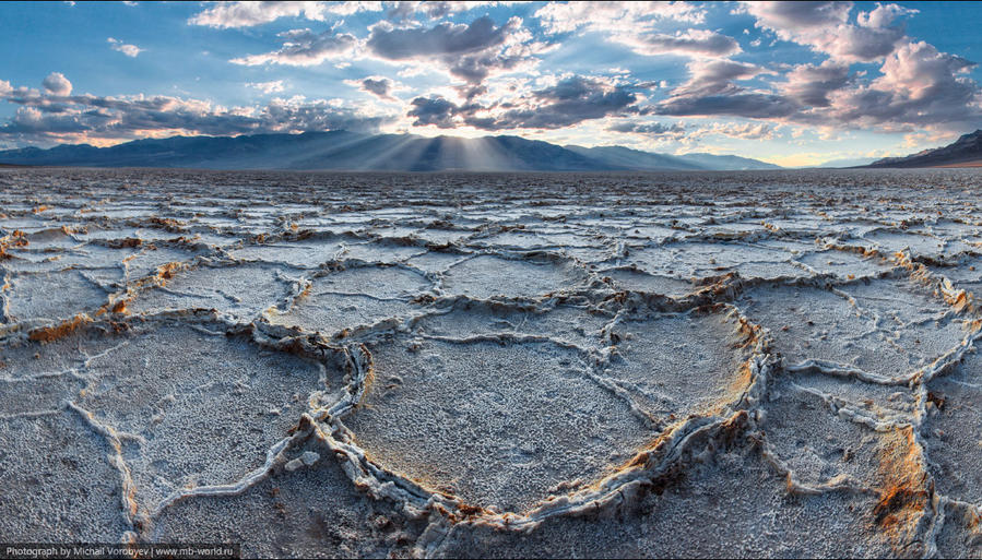 Badwater Basin
Заключительное место в Долине смерти которые мы успели посетить.
Именно здесь расположена самая низкая точка Северной Америке – 87 м ниже уровня моря. Об этом свидетельствует табличка которая вида если поднять взгляд на отвесную гору у паркинга.
Но место знаменито не этим. А удивительной поверхностью образованной толстым слоем соли, который складывается в причудливые узоры.
Несколько тысяч лет назад здесь плескалось озеро Lake Manly, но сегодня оно исчезло оставив после себя лишь соль.
Своим названием Badwater (что значит “Плохая вода”) это место обязано опять же пионерам освоения Запада. Когда здесь появились первые исследователи, измученные жаждой они увидели небольшие лужи воды, что скапливается среди соляных узоров. Но выпив глоток, морщась выплевывали, с криками Bad water! (“Плохая вода!”)
Все дело в том, что вода содержит большое количество концентраций хлоридов, сульфатов и натрия, что проявляется во вкусе…