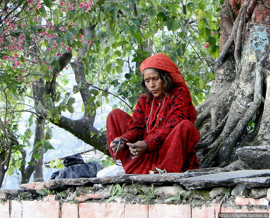 Красное одеяние этой женщины было заметно издалека. С утра она  памятником сидела  на постаменте, окружавшем огромное высокое дерево. Уже к вечеру я возвращалась в гостиницу, а она всё сидела, не изменив утренней позы. Ничего не продавала, и подаяния вроде не просила. И чего она ждала.... Покхара, Непал