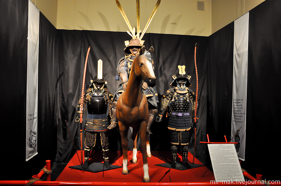 Отряд самураев.

В центре этого небольшого отряда – всадник. Впервые лошади были завезены в Японию с континента в 5 веке, они всегда ценились очень высоко, поэтому только благородные воины (буси) составляли конницу. Животные того времени были очень низкорослыми и обладали необузданным нравом, однако они были чрезвычайно выносливы, удивительно быстроходны и способны к совершению маневров высокой сложности – что особенно важно для Японии с ее горным ландшафтом, испещренным речушками.

Сбрую (багу) японцы во многом заимствовали у китайцев, в нее входят седло кура, подпруга харуби, подушка и стремена абуми, под седло клали потник кицукэ. Управлять лошадью помогали удила куцува, нащечники кангава-ита, нахрапник ханагава и поводья куцу-вадзура.

Интересны представленные доспехи. Слева от всадника доспех клана Отавара 17 века. Такой стиль обмундирования имеет название «намбан» — южные варвары. Кираса намбан нимай-до с цельнометаллической передней пластиной в стиле испанского мориона, с традиционной латной юбкой кусадзури из шести клиньев, состоящих из облегченных посеребренных кожаных пластин, соединенных синим шнуром. Наручи цуцуготэ из металлических трубок, соединенных шарнирными петлями, которые украшены изображениями бабочек, выполненными золотым лаком.

Всадник представлен доспехом клана Мацудайра 18 века. Клан Мацудайра стремительно возвысился в 16 веке, когда во главе его встал Мацудайра Мотояси – впоследствии сменивший имя на Токугава Иэясу. Он завершил процесс объединения раздробленной феодальной Японии и стал первым из сегунов Токугава, управлявших страной до 1868 года.

И третий доспех с гербом маару-ни-ити (горизонтальная полоса в круге) конца 18 века представляет собой классический доспех тосэй гусоку. Такое обмундирование было характерным для каждого военного князя эпохи воюющих провинций в конце 16 века. Одесса, Украина