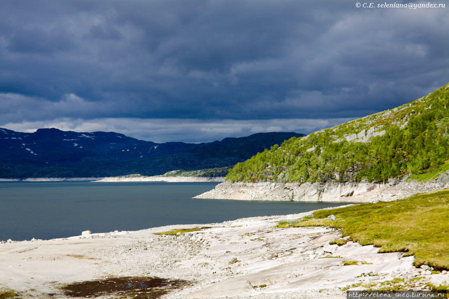 10.  Фантасмагорическая картина. Буквально на полминуты солнце вдруг ярко осветило этот край озера с белым берегом, ещё сильнее оттенив тёмные синие тучи, нависшие над озером. Берег вовсе не песчаный, как можно подумать, но вот отчего-то белый. Удивительно. Норвегия